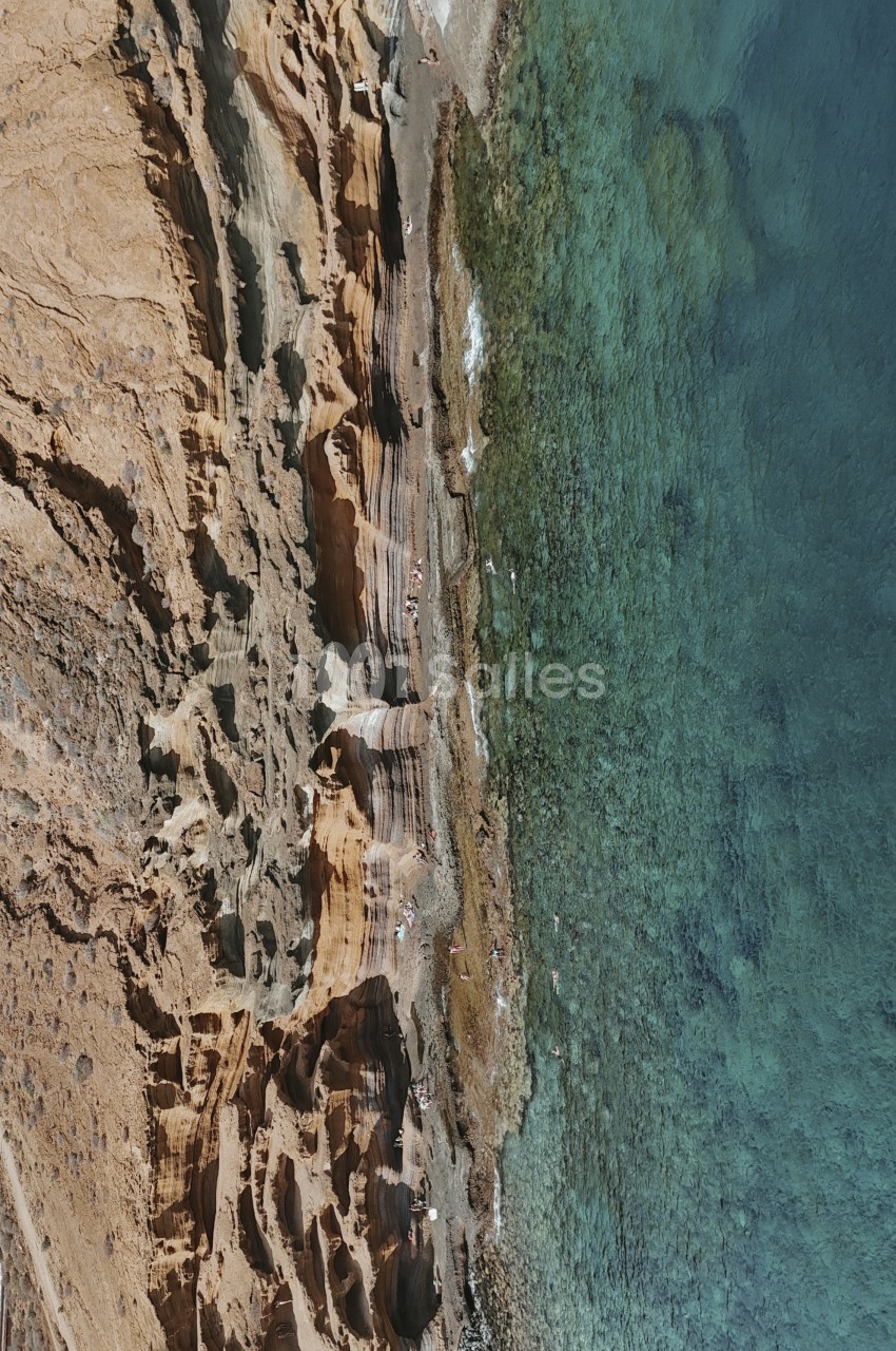 Falaise rocheuse surplombant une eau turquoise avec une personne sur la plage de galets.