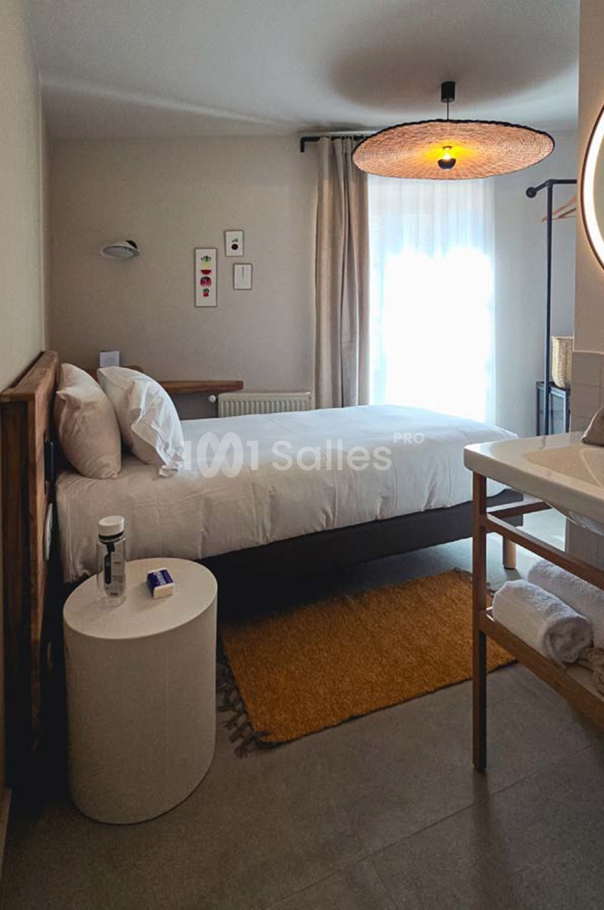 Chambre d'hôtel avec lit queen-size, luminaire suspendu en rotin, fenêtre donnant sur l'extérieur et mobilier en bois clair.
