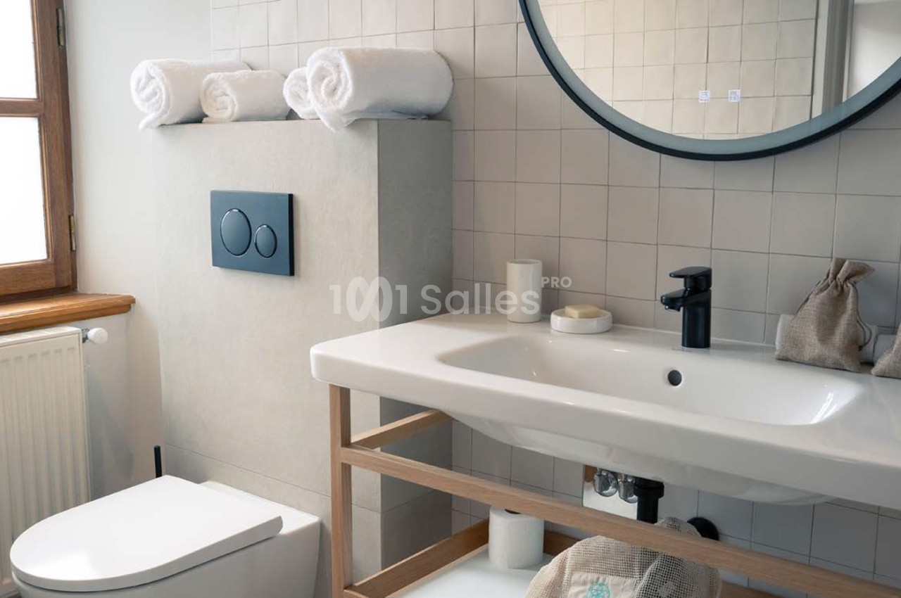 Salle de bains moderne avec lavabo blanc, toilettes, miroir rond et serviettes roulées.