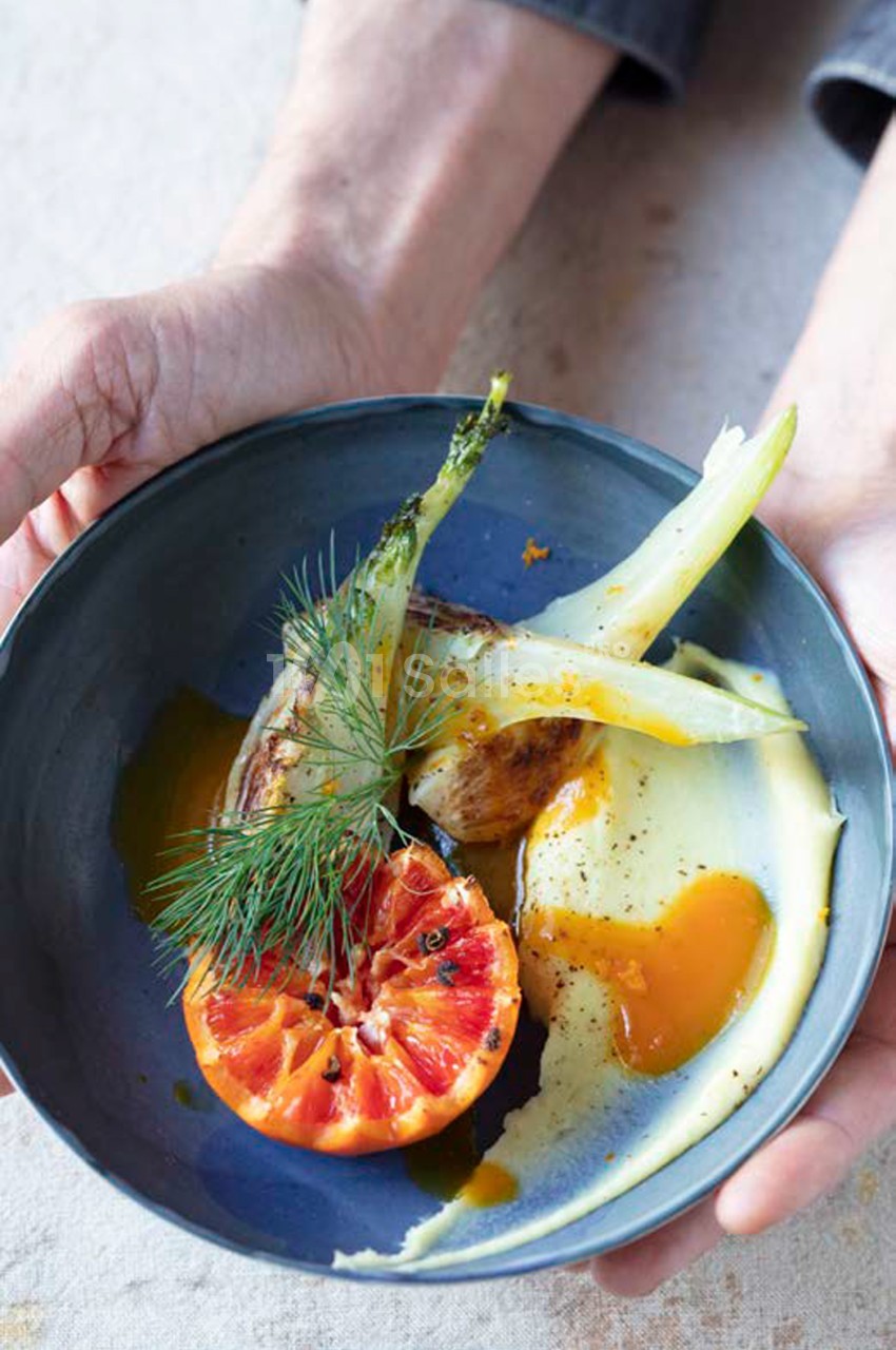 Assiette bleue tenue en main contenant pamplemousse, œuf et herbes aromatiques.