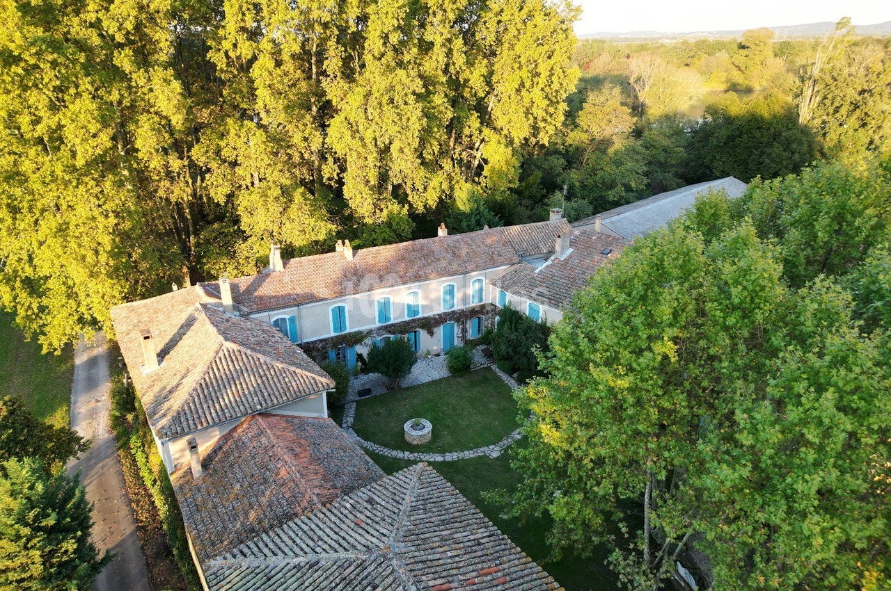 Vue aérienne d'une grande maison en pierre avec toit en tuiles, entourée d'arbres et d'un jardin central.