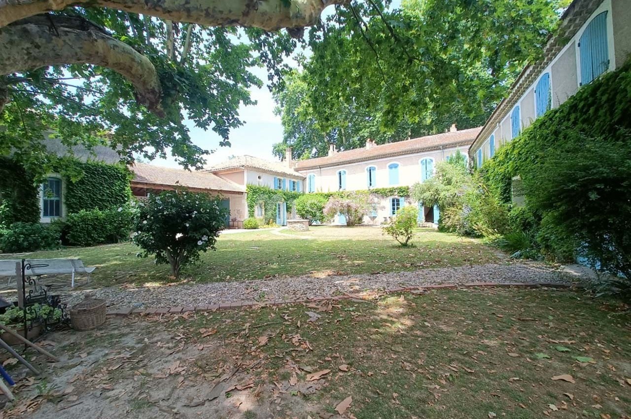 Cour intérieure d'une maison traditionnelle entourée de murs en pierre couverts de végétation et d'arbres.