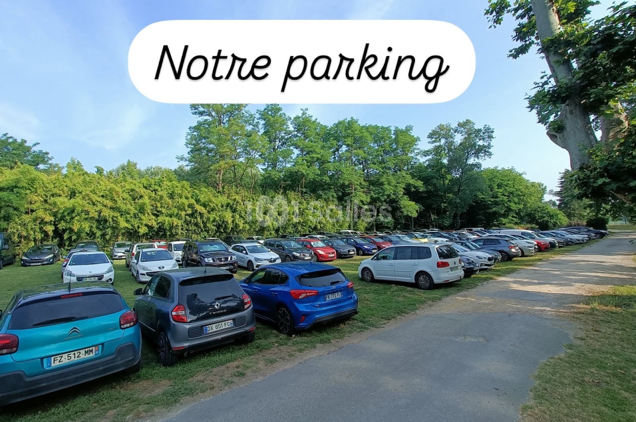 Un parking extérieur avec plusieurs voitures stationnées, entouré de verdure et d'arbres sous un ciel dégagé.