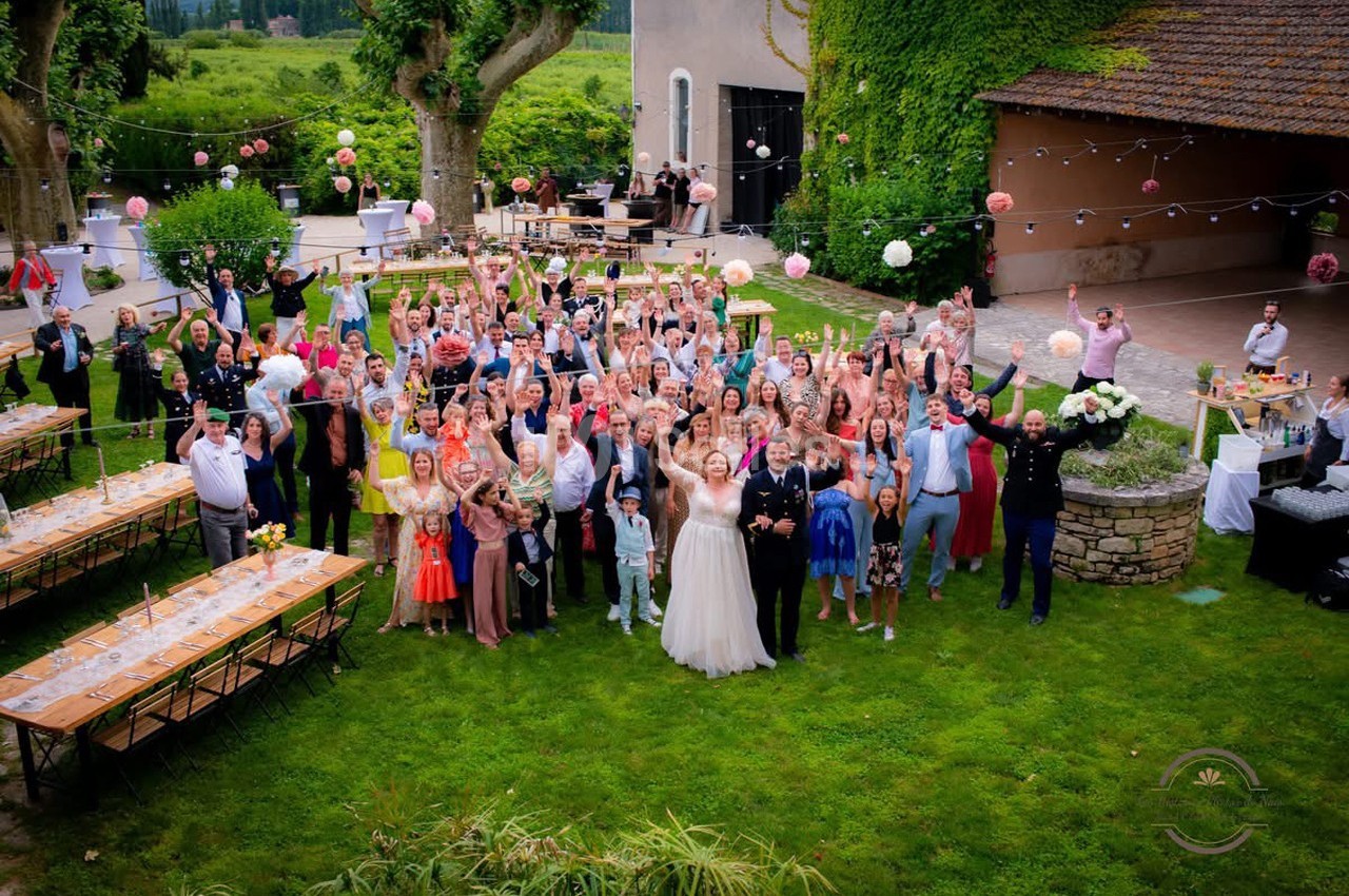 Un groupe de personnes rassemblées dans un jardin pour une célébration, avec des tables dressées et des décorations…