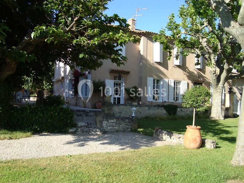 Maison en pierre avec volets blancs, entourée d'arbres et d'un jardin, sous un ciel bleu ensoleillé.