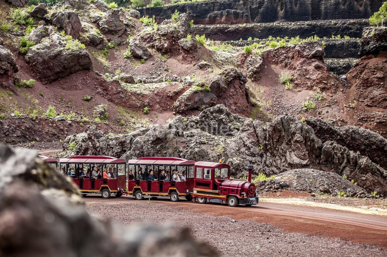 Petit train touristique rouge transportant des passagers à travers un paysage rocheux et volcanique.