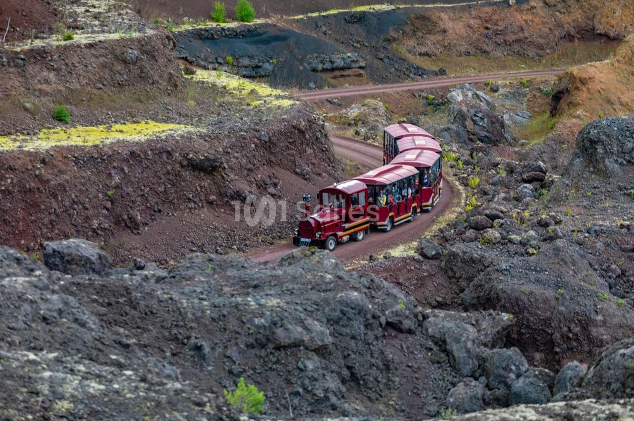 Petit train rouge transportant des passagers sur un chemin sinueux au milieu d'un paysage volcanique rocheux.