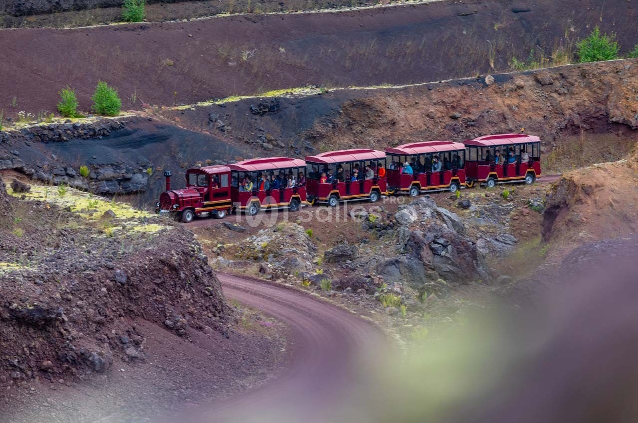 Petit train touristique rouge transportant des passagers sur un chemin sinueux dans un paysage volcanique.