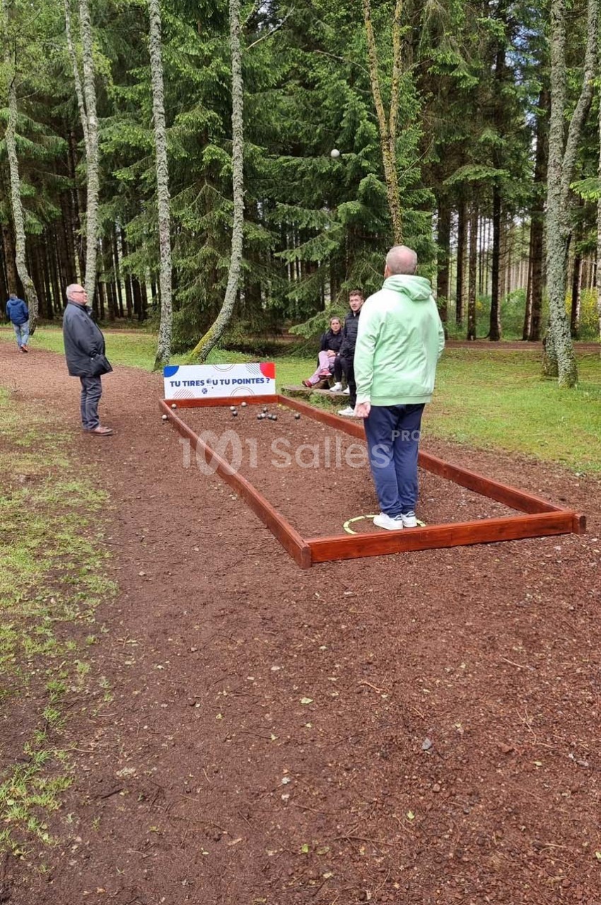 Une personne en vert joue à un jeu d'équilibre sur une poutre en bois dans un parc boisé, sous le regard d'autres…