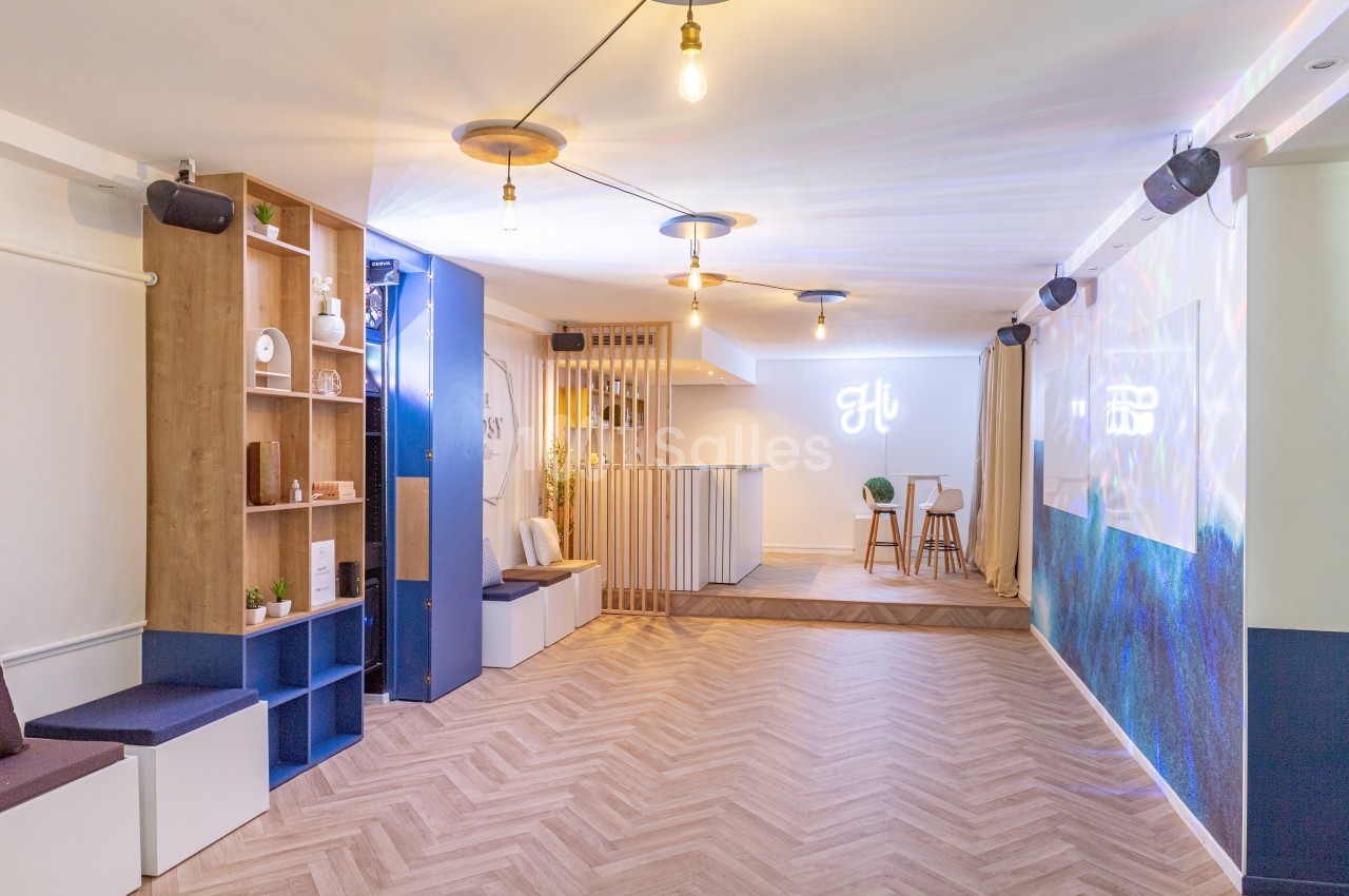 Salle lumineuse avec parquet en chevrons, bar moderne, étagères en bois et éclairage suspendu.