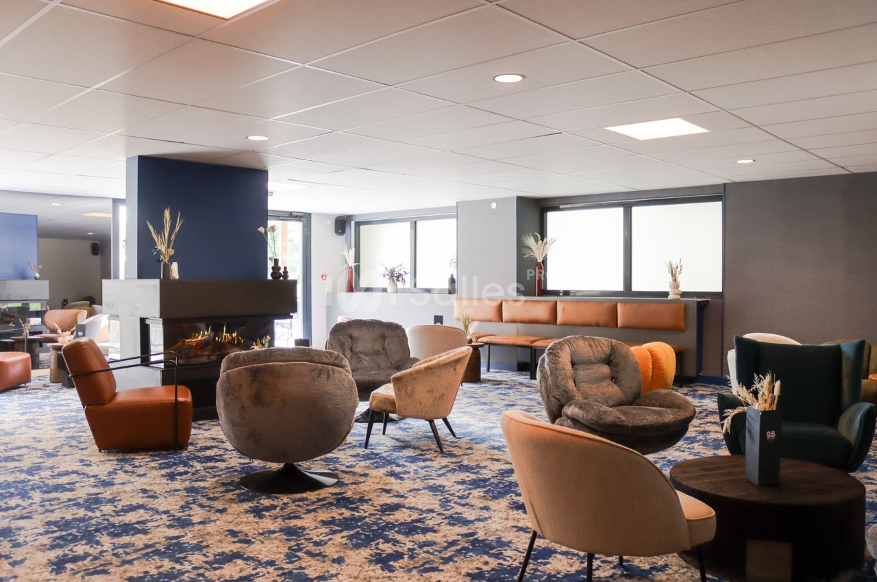 Espace salon moderne avec fauteuils variés, cheminée centrale et grandes fenêtres laissant entrer la lumière naturelle.