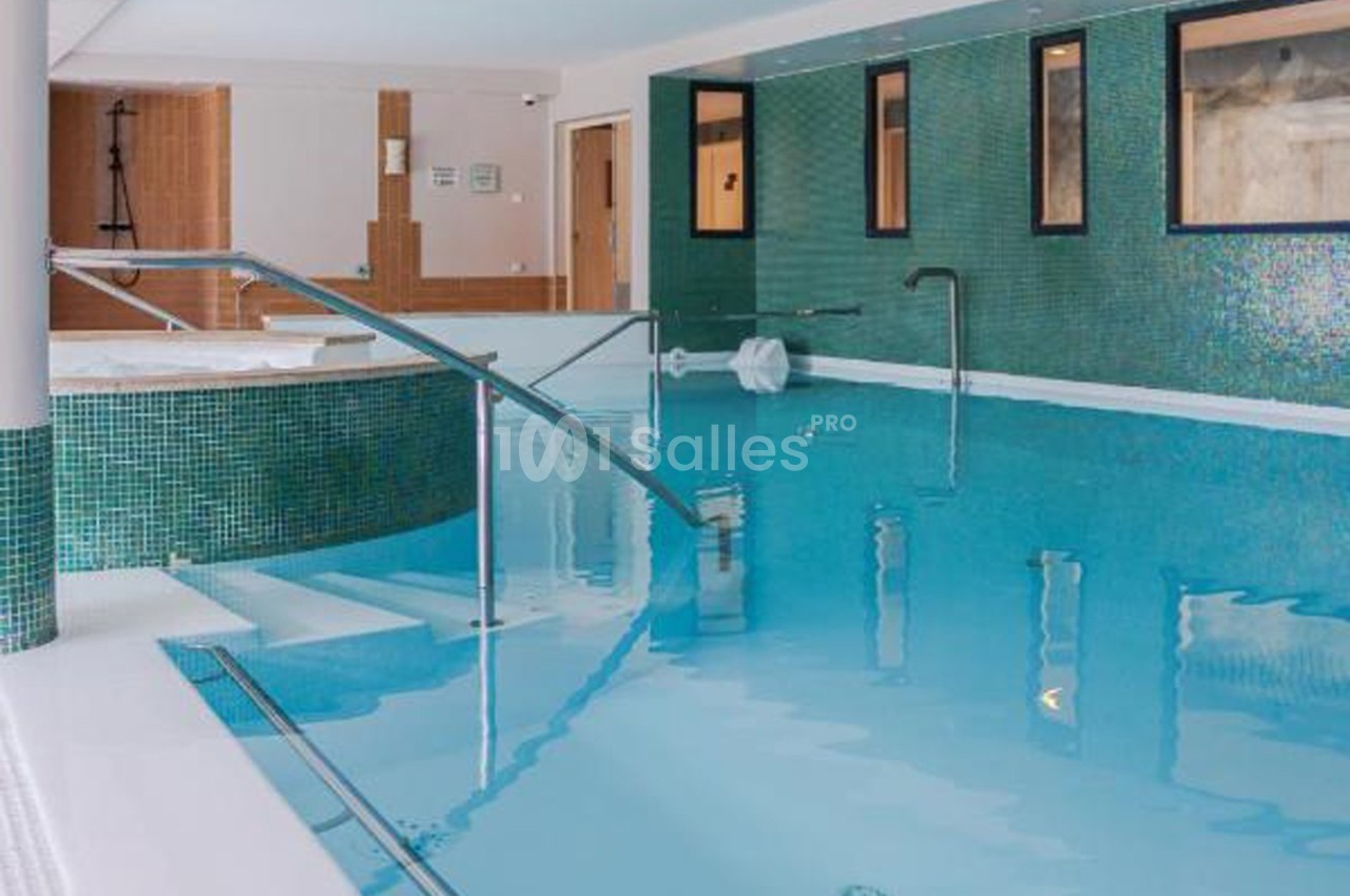 Piscine intérieure avec eau claire, carrelage vert, rampes d'accès métalliques et espace spa en arrière-plan.