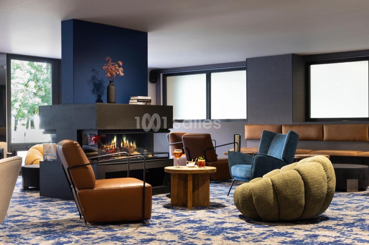 Espace salon moderne avec cheminée, fauteuils variés, table basse et grandes fenêtres laissant entrer la lumière naturelle.