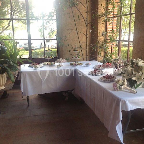 Tables décorées avec nappes blanches, disposant de plats et desserts, dans un espace lumineux avec des plantes en arrière…