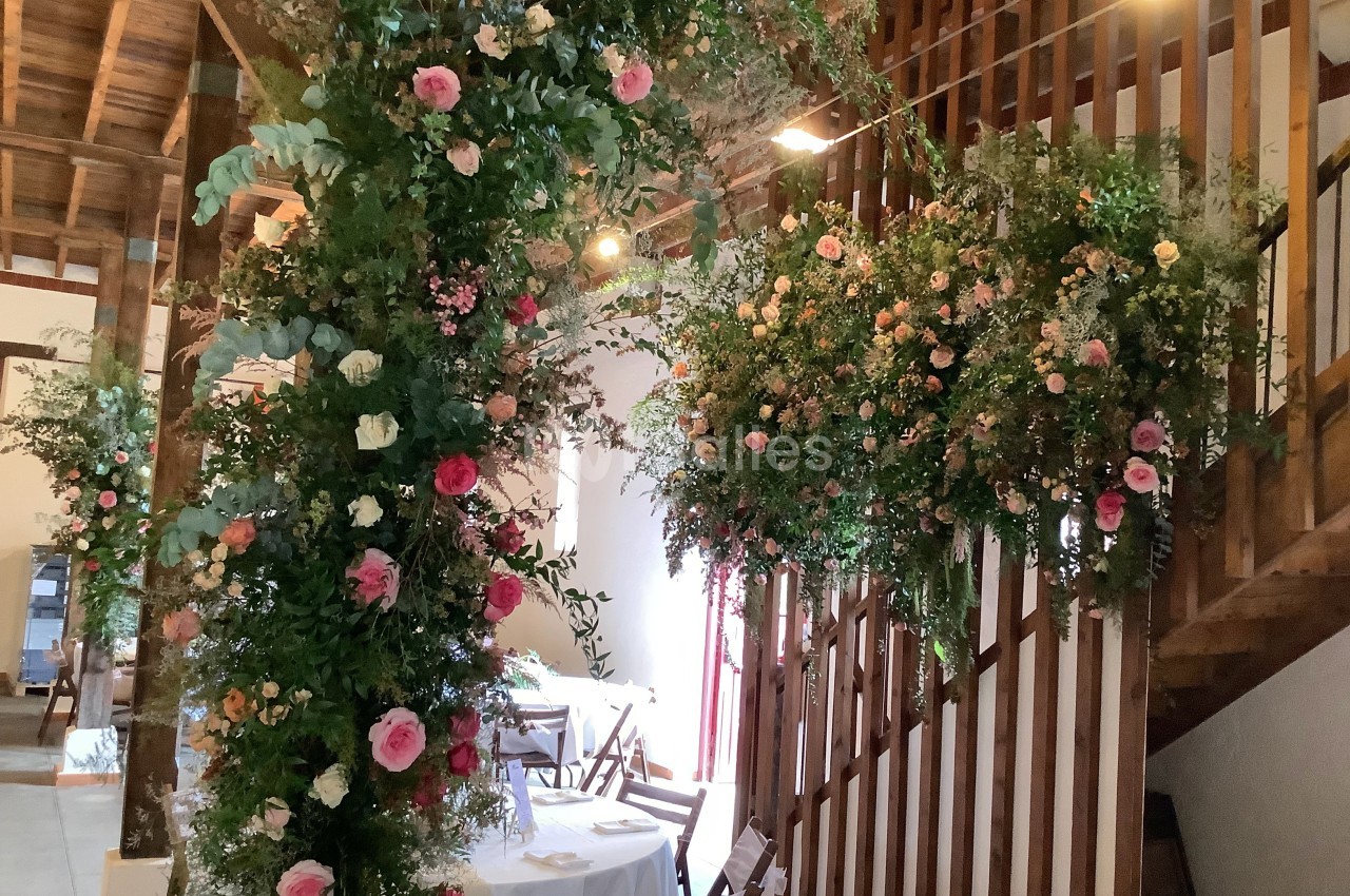 Décoration florale abondante avec des roses et feuillages suspendus dans une salle au plafond en bois.