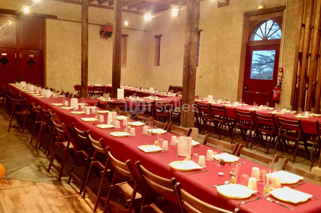 Salle de réception avec de longues tables dressées de nappes rouges, alignées avec des chaises en bois.