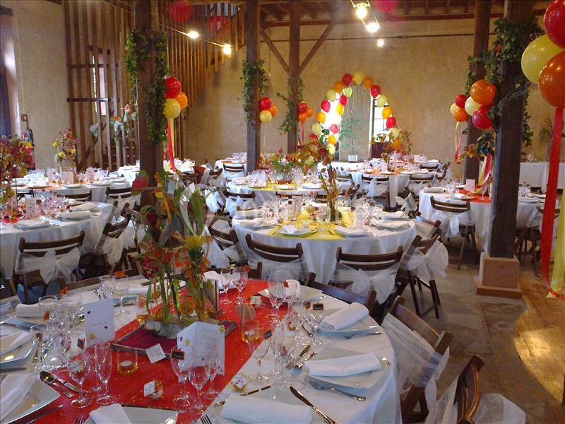 Salle décorée pour un événement avec des tables rondes dressées, ornées de nappes rouges et de compositions florales.