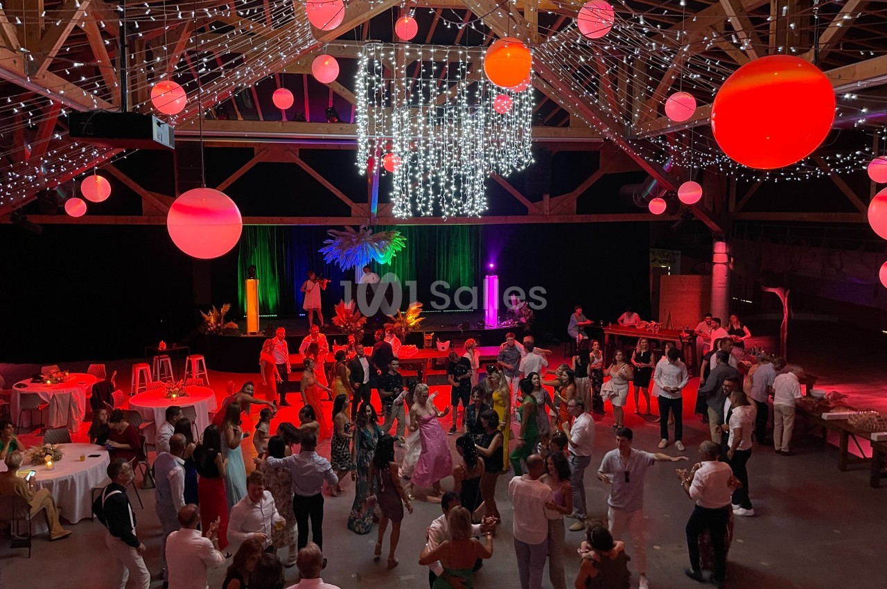 Salle festive avec des invités dansant sous des lumières colorées, des décorations suspendues et des tables disposées autour.
