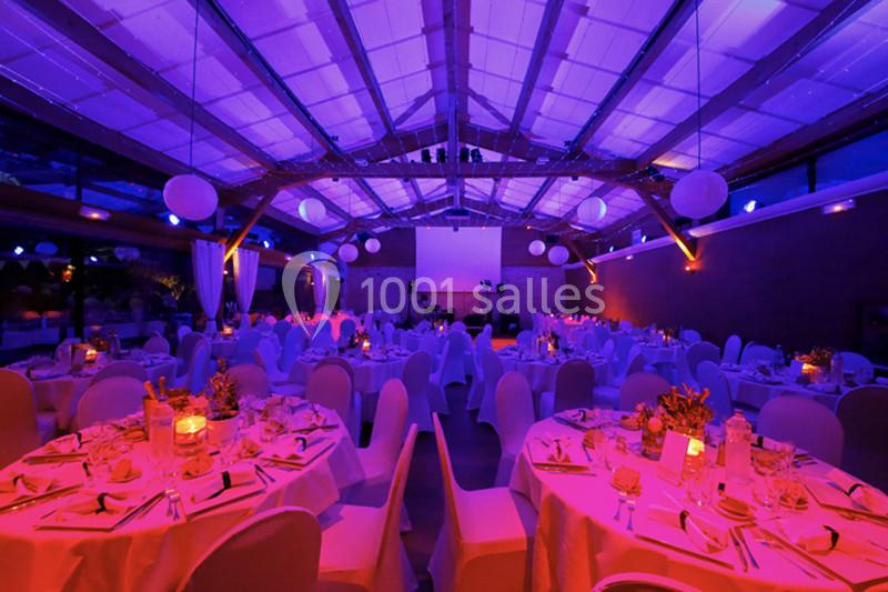 Salle de réception décorée avec des tables rondes dressées, éclairage violet et ambiance festive.