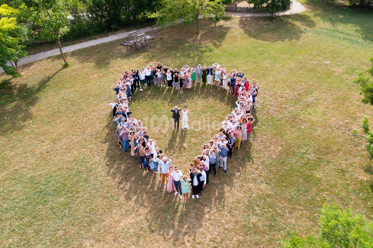 Vue aérienne d'un groupe de personnes formant un cœur autour d'un couple au centre, dans un parc verdoyant.