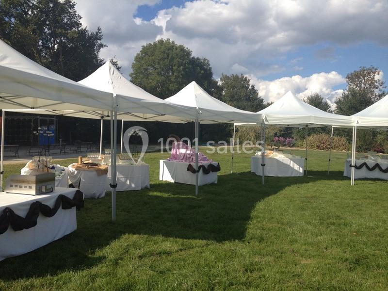 Tentes blanches alignées sur une pelouse, abritant des tables décorées pour un événement en plein air.