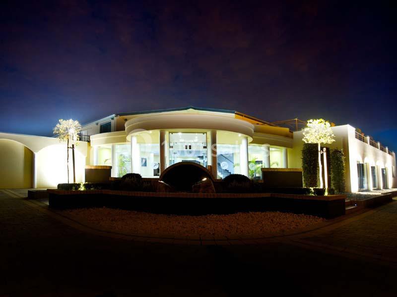 Façade d'une maison moderne éclairée la nuit, avec des arbres illuminés et une entrée centrale vitrée.