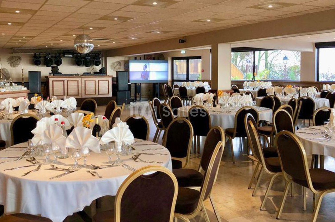 Salle de réception avec tables rondes dressées, nappes blanches, serviettes pliées et décoration élégante.