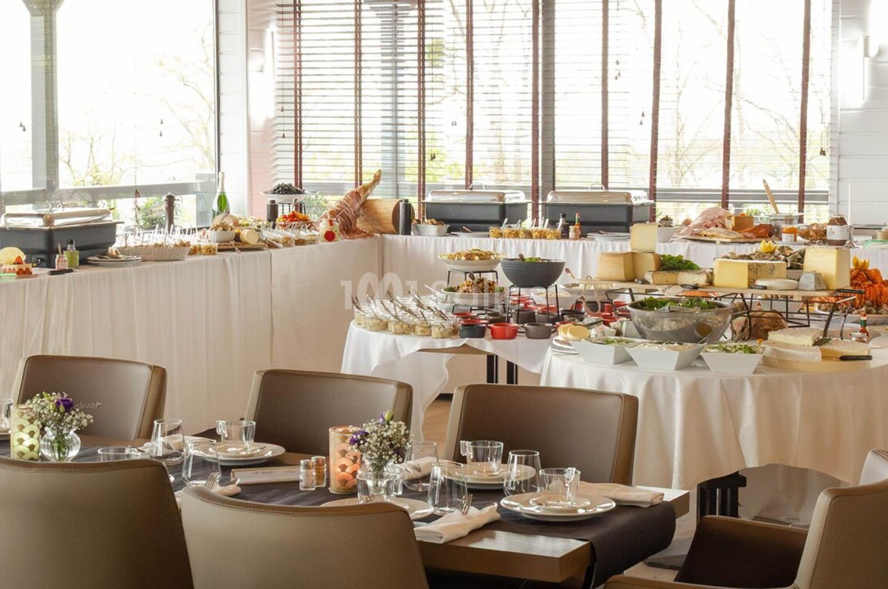 Salle de restaurant avec tables dressées et buffet varié comprenant fruits, fromages et desserts.