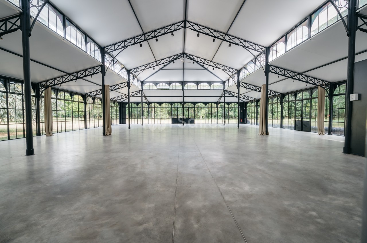 Intérieur d'une grande salle lumineuse avec structure métallique, murs vitrés et sol en béton poli.