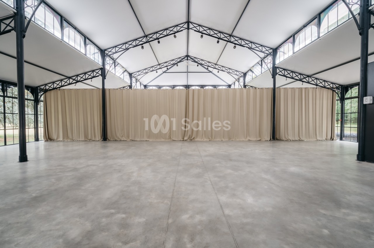 Intérieur d'une grande salle avec structure métallique, sol en béton et rideaux beiges couvrant un mur.