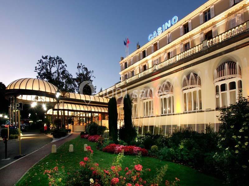 Façade éclairée d'un casino entouré de jardins fleuris, photographiée à la tombée de la nuit.