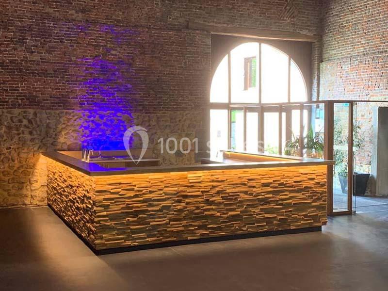 Comptoir en bois éclairé dans un espace intérieur avec murs en briques et grande baie vitrée en arrière-plan.