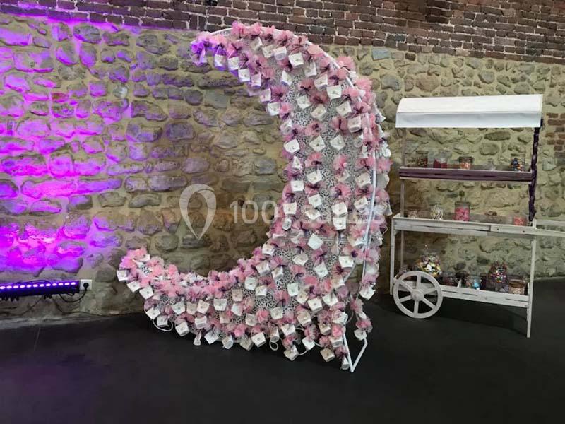 Structure en forme de croissant de lune décorée de fleurs roses et de cartes, devant un mur en pierre.