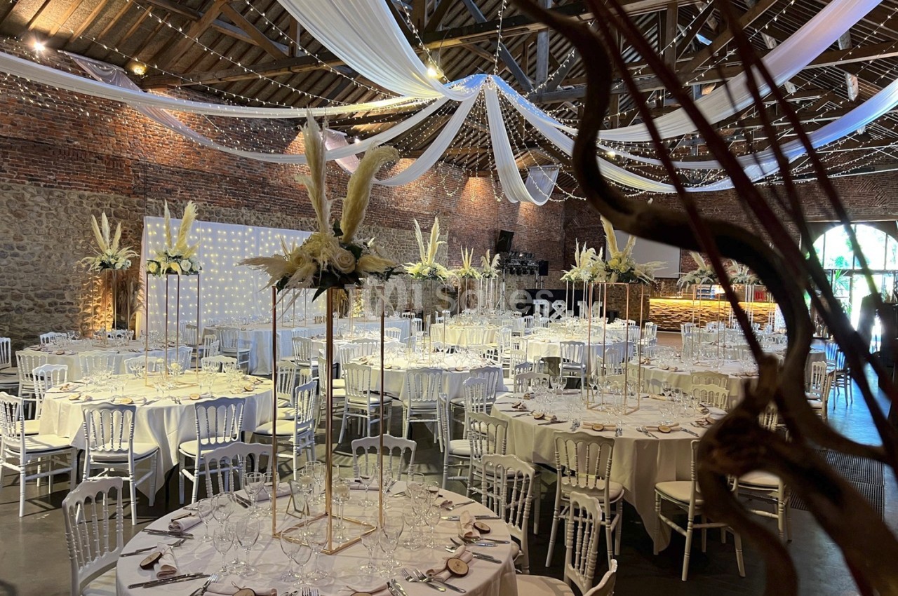 Salle de réception décorée pour un mariage, avec tables rondes, nappes blanches et ornements floraux élégants.