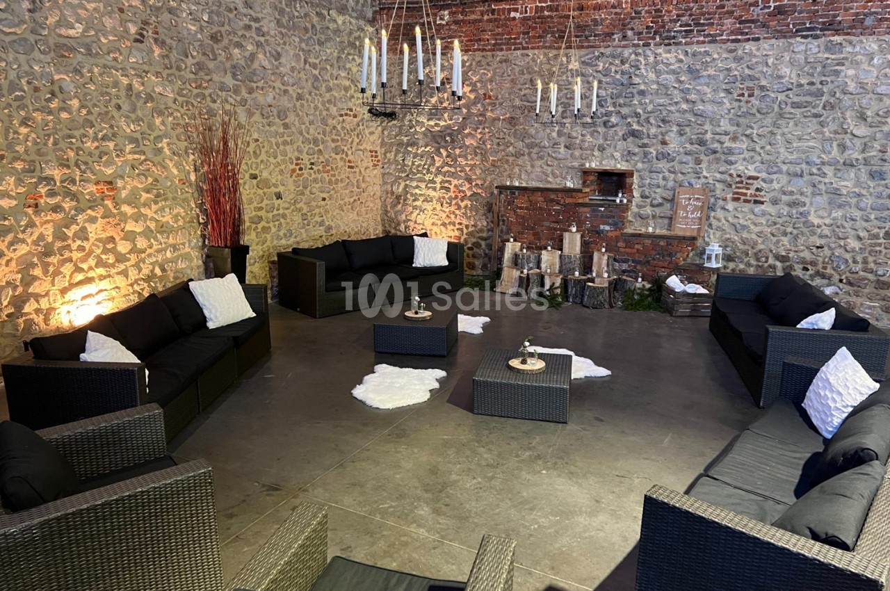 Espace lounge avec canapés en rotin noir, tables basses et décoration rustique dans une salle aux murs en pierre.