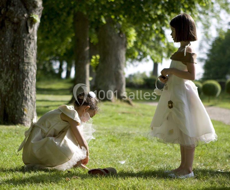 Deux jeunes filles en robes élégantes jouent sur une pelouse verdoyante, entourées d'arbres par une journée ensoleillée.