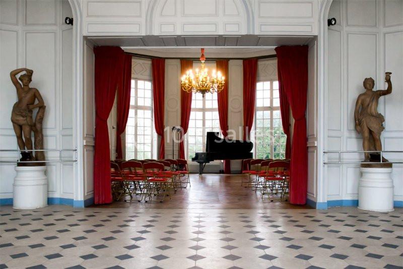 Salle élégante avec un piano à queue, des chaises alignées, des rideaux rouges et des statues décoratives.