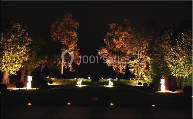 Allée de jardin éclairée la nuit, bordée d'arbres illuminés et décorée de statues lumineuses en forme de cerfs.