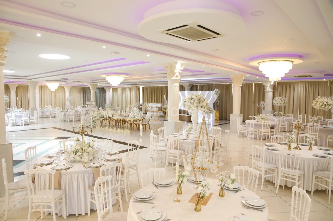 Salle de réception élégante avec tables rondes décorées de blanc, chaises assorties et éclairage lumineux.