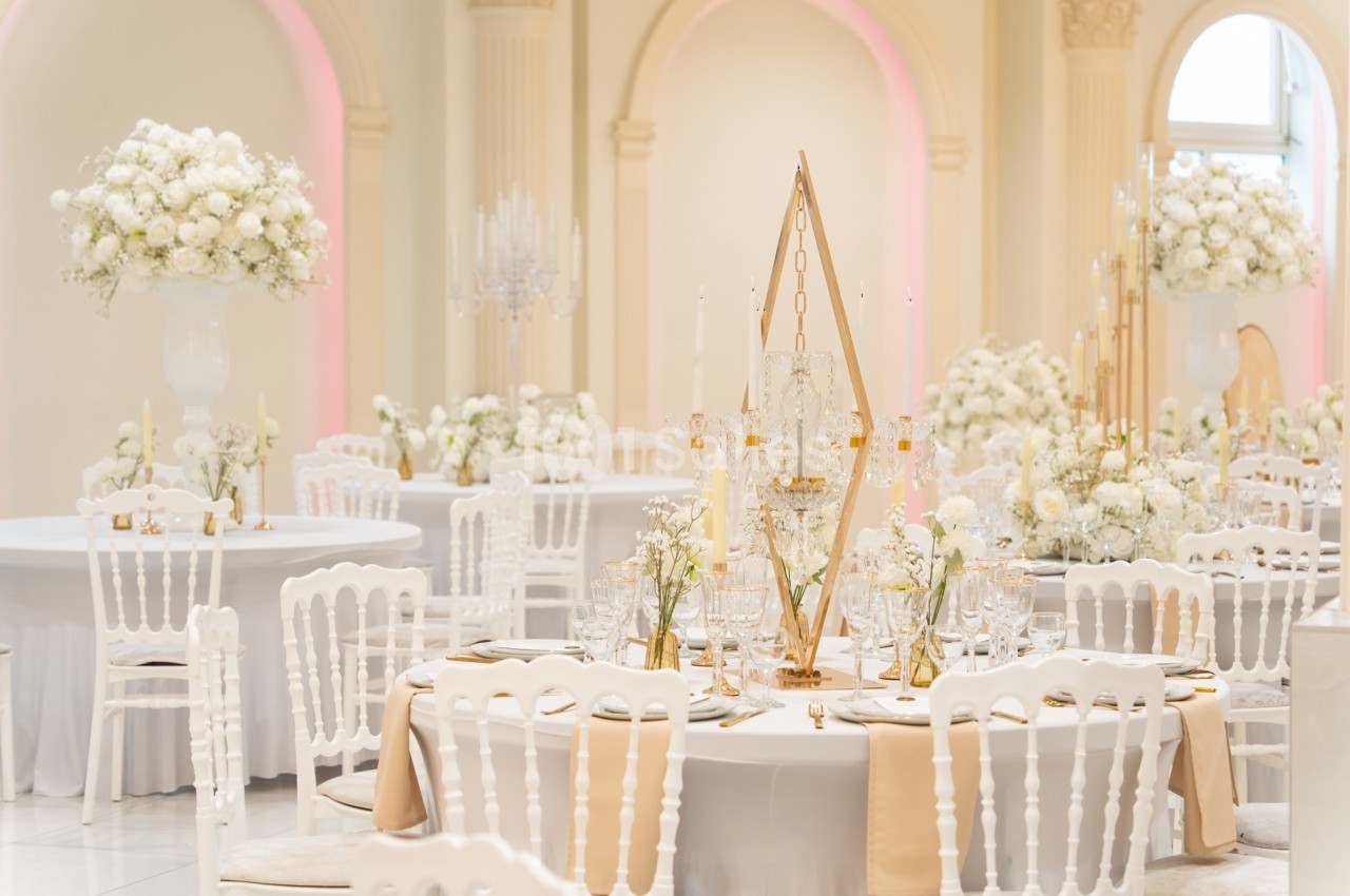 Salle de réception élégante avec tables décorées de fleurs blanches, chaises blanches et lumière douce.