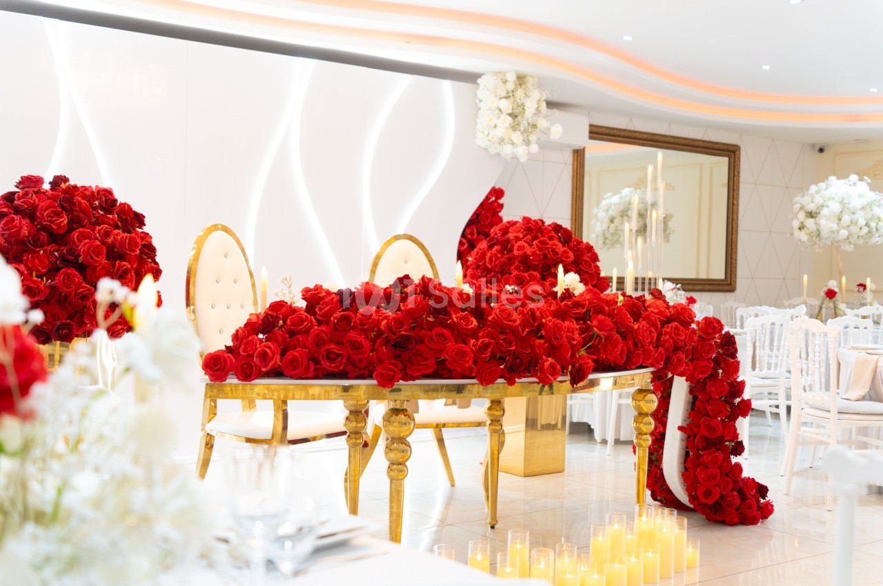 Table ornée de roses rouges avec chaises dorées, bougies et décorations florales dans une salle de réception élégante.