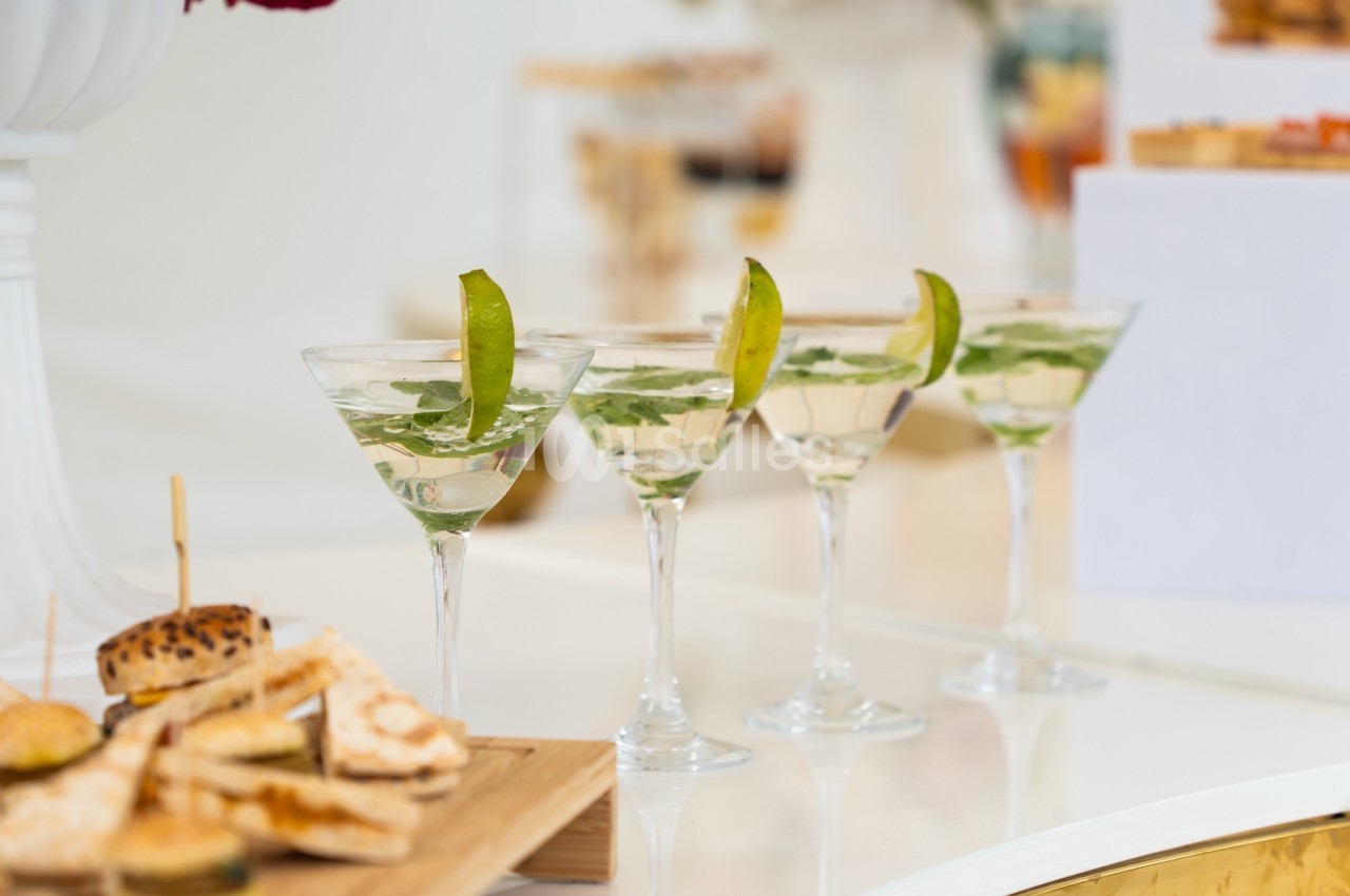 Quatre verres de cocktail garnis de feuilles de menthe et de tranches de citron vert, posés sur une table blanche.