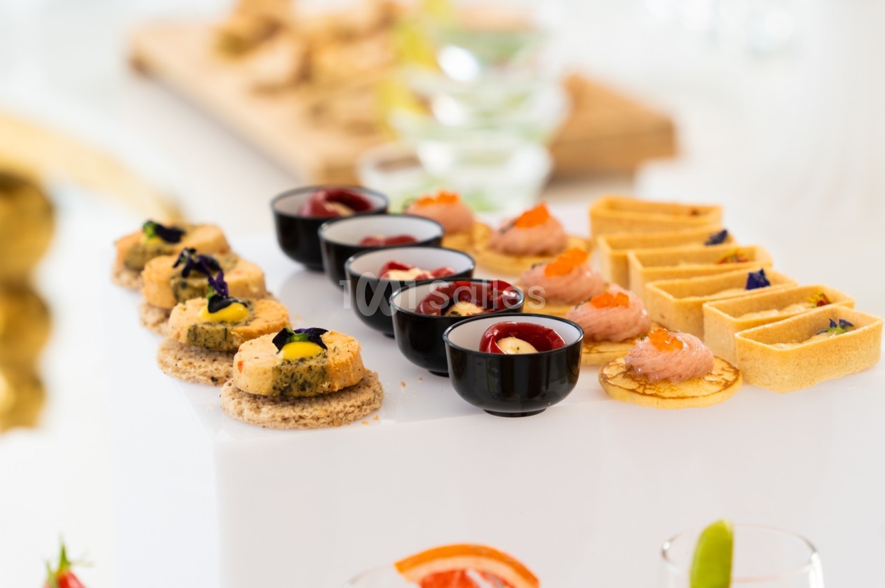 Assortiment de canapés et amuse-bouches variés présentés sur un plateau blanc lors d'un événement ou d'un buffet.