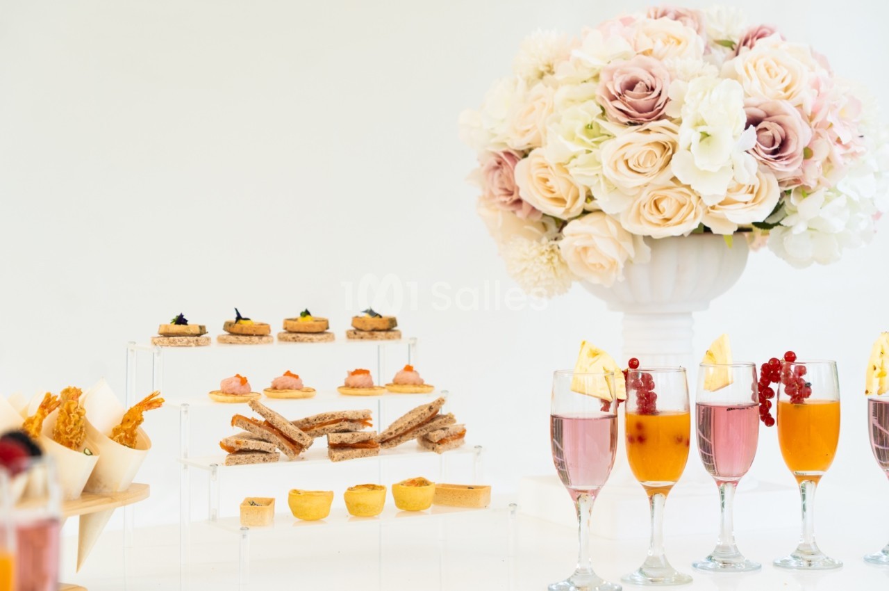 Buffet élégant avec amuse-bouches, verrines colorées et un bouquet de fleurs pastel en arrière-plan.