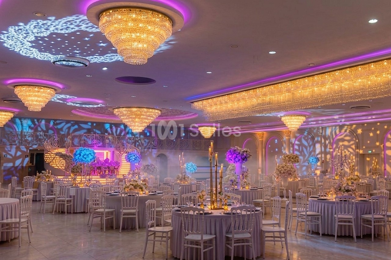 Salle de réception élégante avec tables décorées, lustres imposants et éclairage d'ambiance coloré.