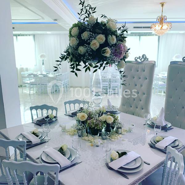 Table élégamment dressée pour un événement, décorée de roses blanches et d'un grand bouquet central.