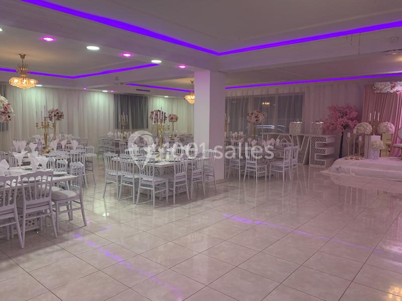 Salle de réception élégante avec tables dressées, chaises blanches et éclairage violet tamisé.