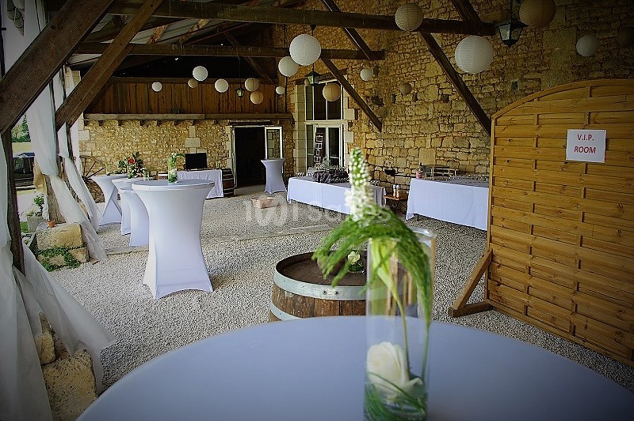 Salle rustique en pierre avec tables hautes décorées, lanternes suspendues et panneau indiquant une salle VIP.