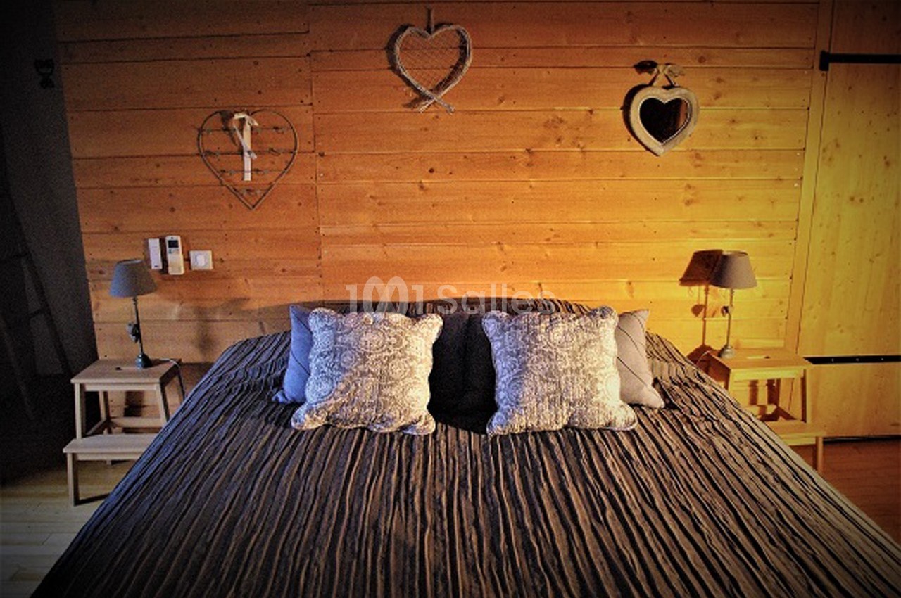 Lit double avec couvre-lit sombre, coussins décoratifs et mur en bois orné de cœurs en décoration murale.