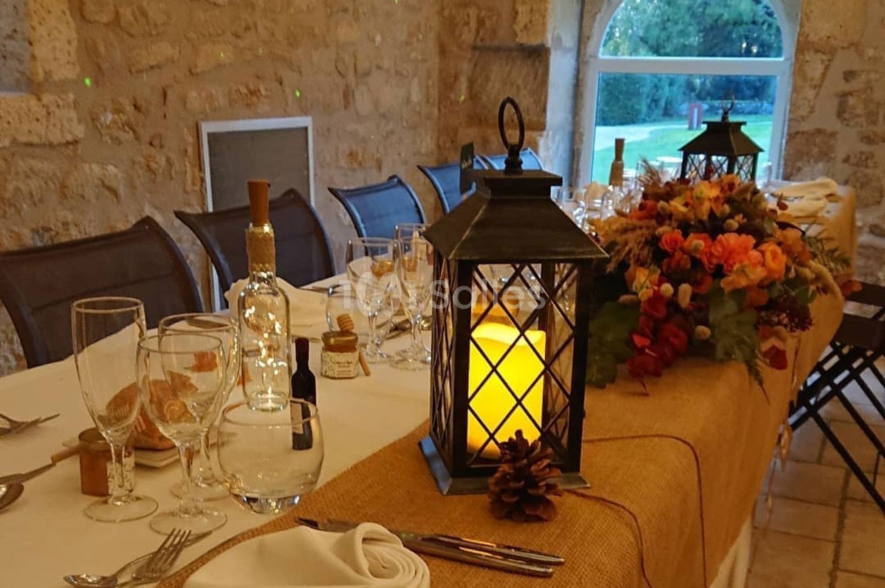 Table décorée pour un repas, avec lanterne allumée, bouquet de fleurs automnales et vaisselle élégante dans une salle en…